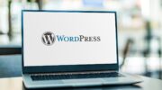 На столі знаходиться ноутбук де на білому фоні освітлюється назва Wordpress з логотипом лівого боку.